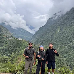 Three trekkers and guides posing on trail with lush valley behind