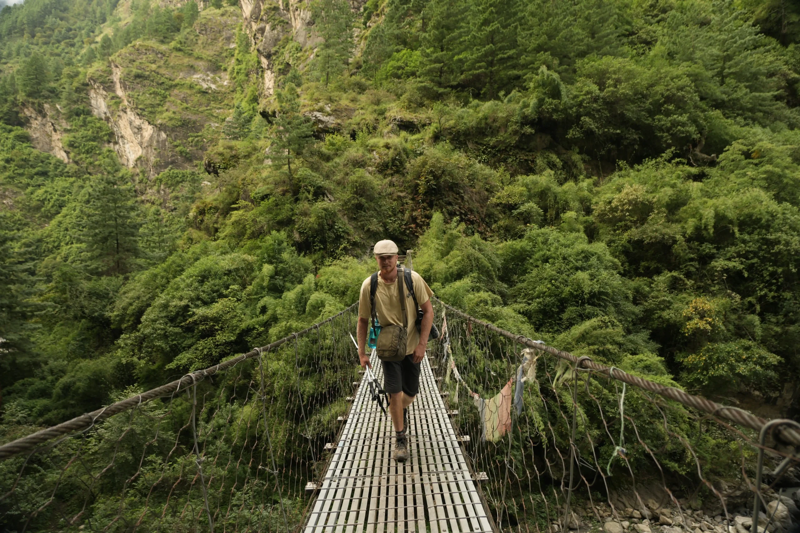 Trekker crossing a suspension bridge over a deep green gorge